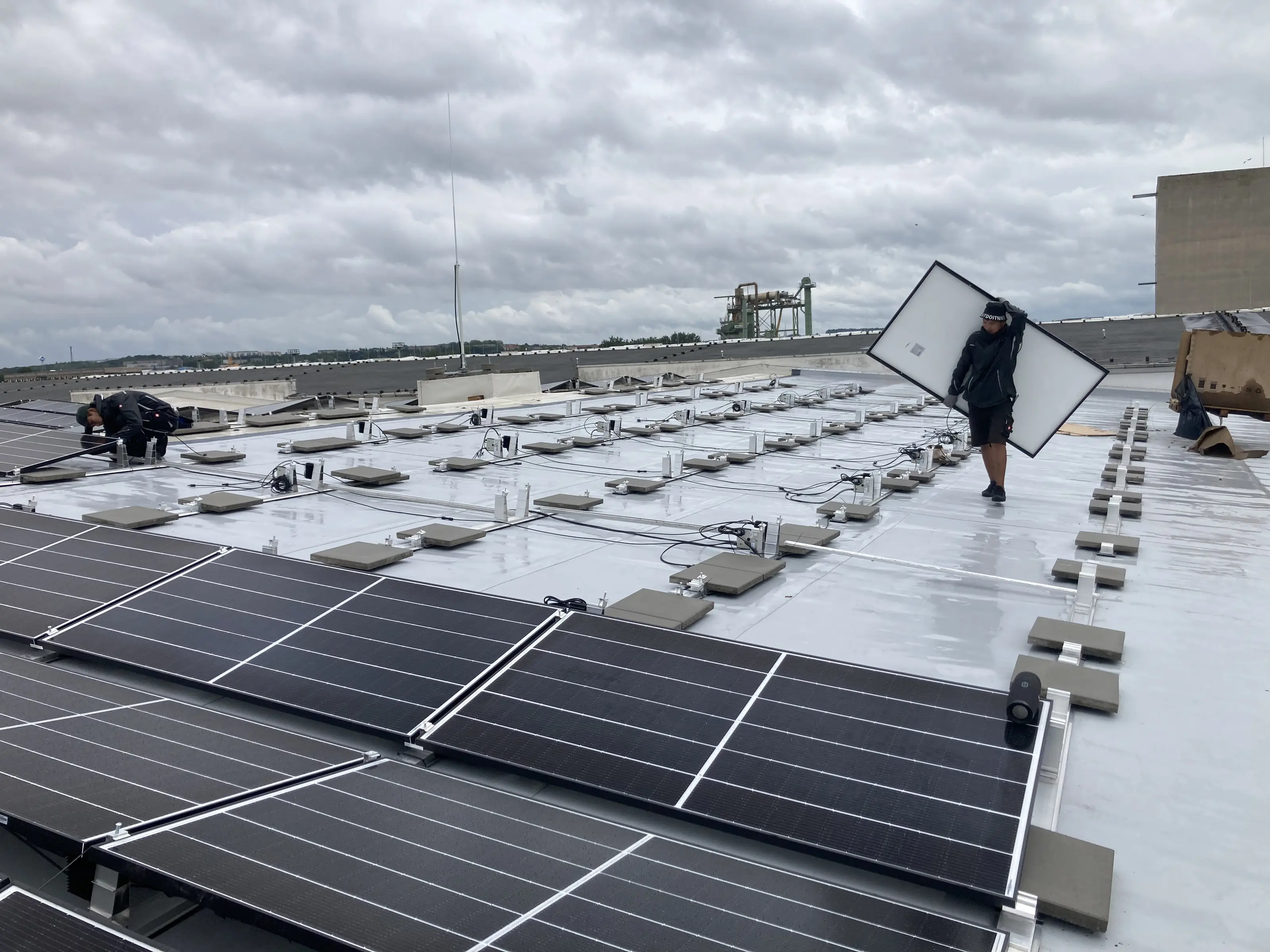 Monteur trägt ein Photovoltaikmodul über ein Flachdach
